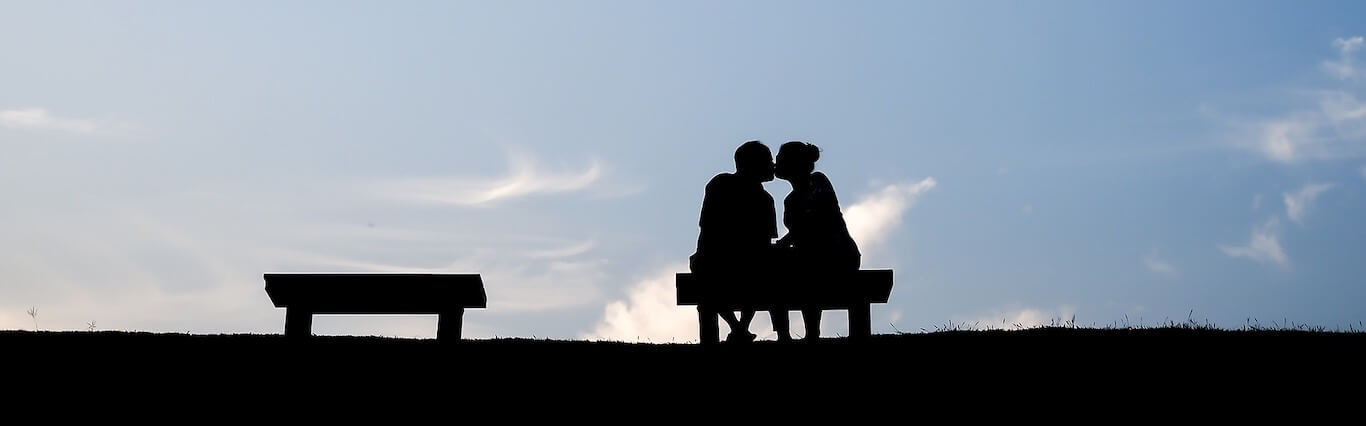 A couple sitting on a bench kissing